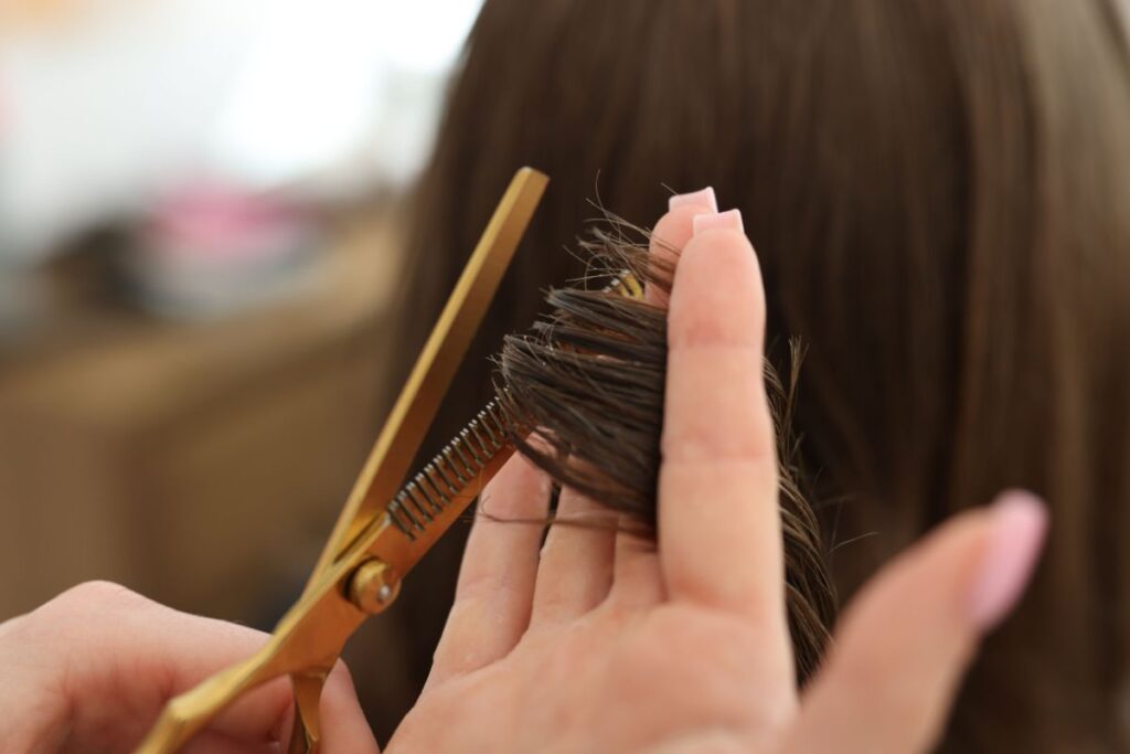 Close-up of a person using scissors to trim the ends of brown hair, with the hair held between the fingers.