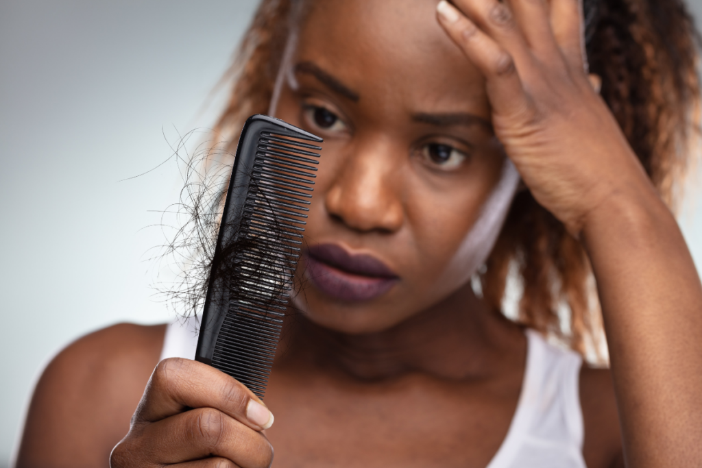Woman looking concerned while holding a comb filled with shed hair, illustrating hair loss and thinning hair concerns.