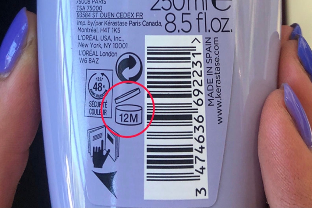 Close-up of a hand holding a product bottle, showing a barcode and an icon indicating the product is good for 12 months after opening.