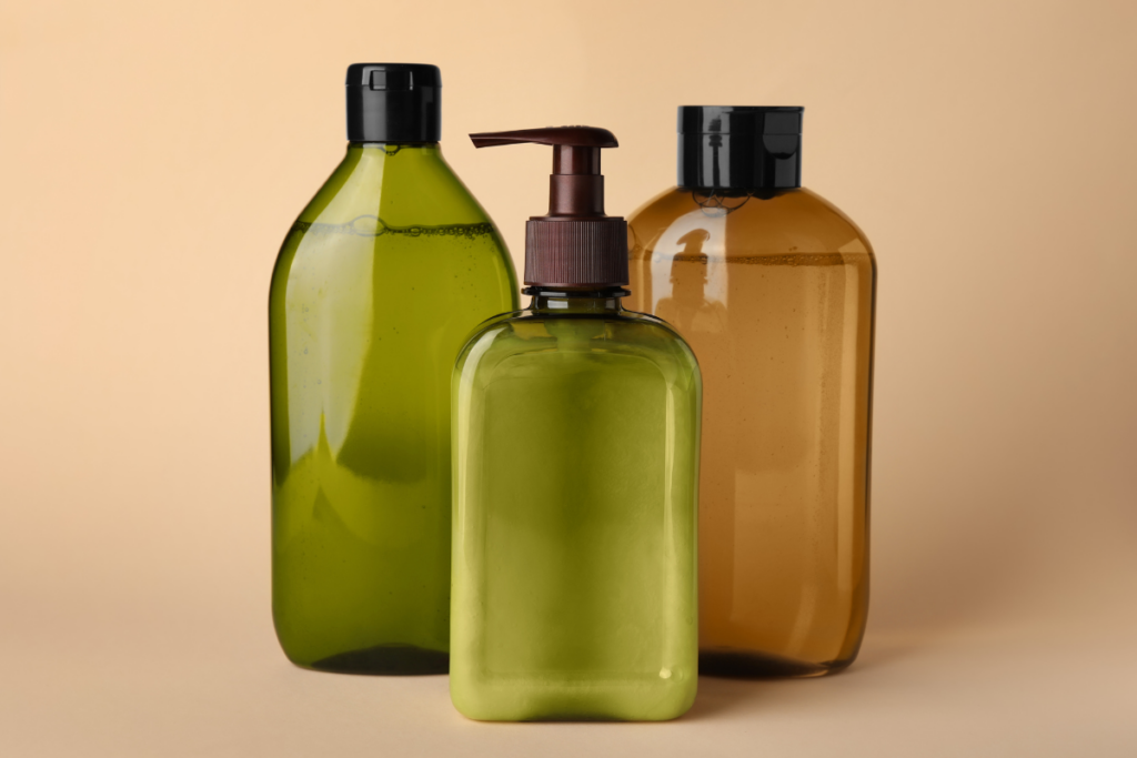 Three plastic bottles, two green with black caps and one brown with a pump dispenser, are displayed against a beige background.