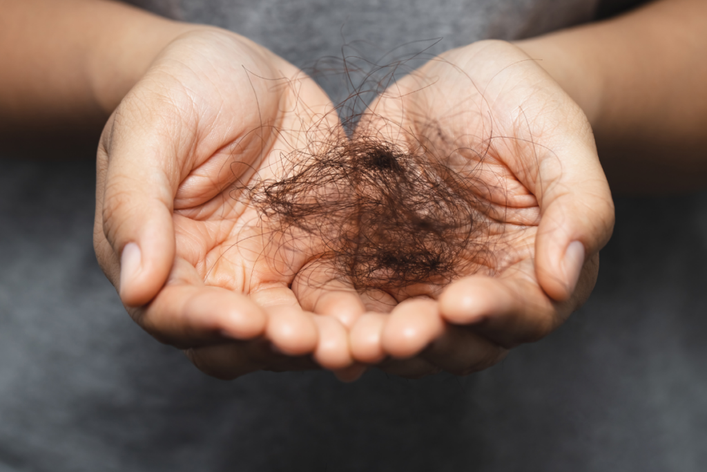 A person holding a clump of dark hair in their cupped hands, illustrating hair loss or shedding.