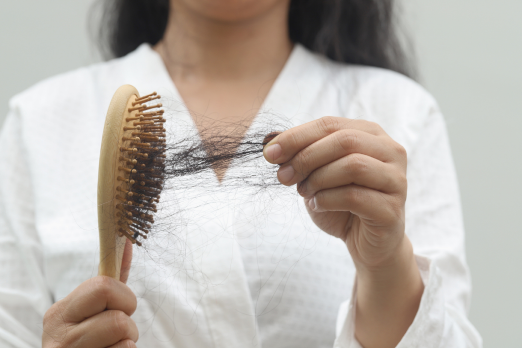 A person in a white shirt holds a wooden hairbrush with a clump of hair tangled in the bristles, indicating hair loss.