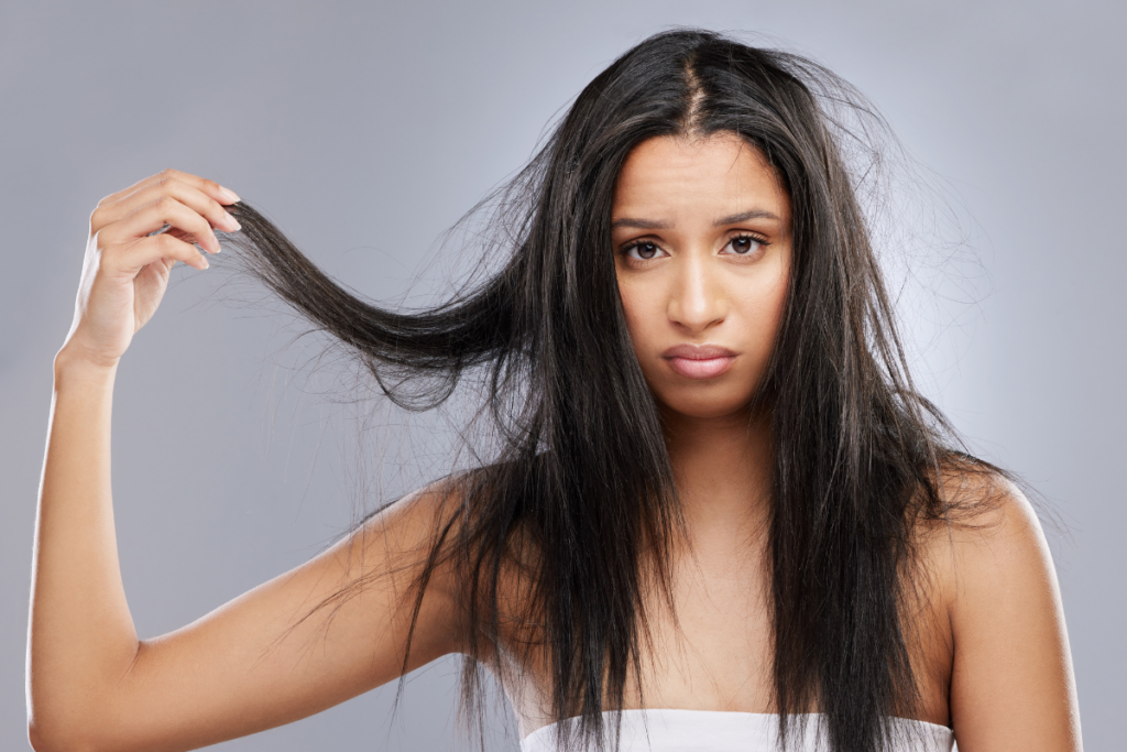 Woman looking toward the camera while holding a section of long dark hair against a gray background.